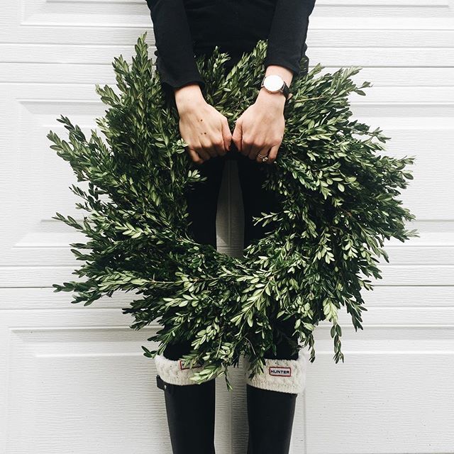 a woman standing in front of a white garage door holding a wreath with her hands