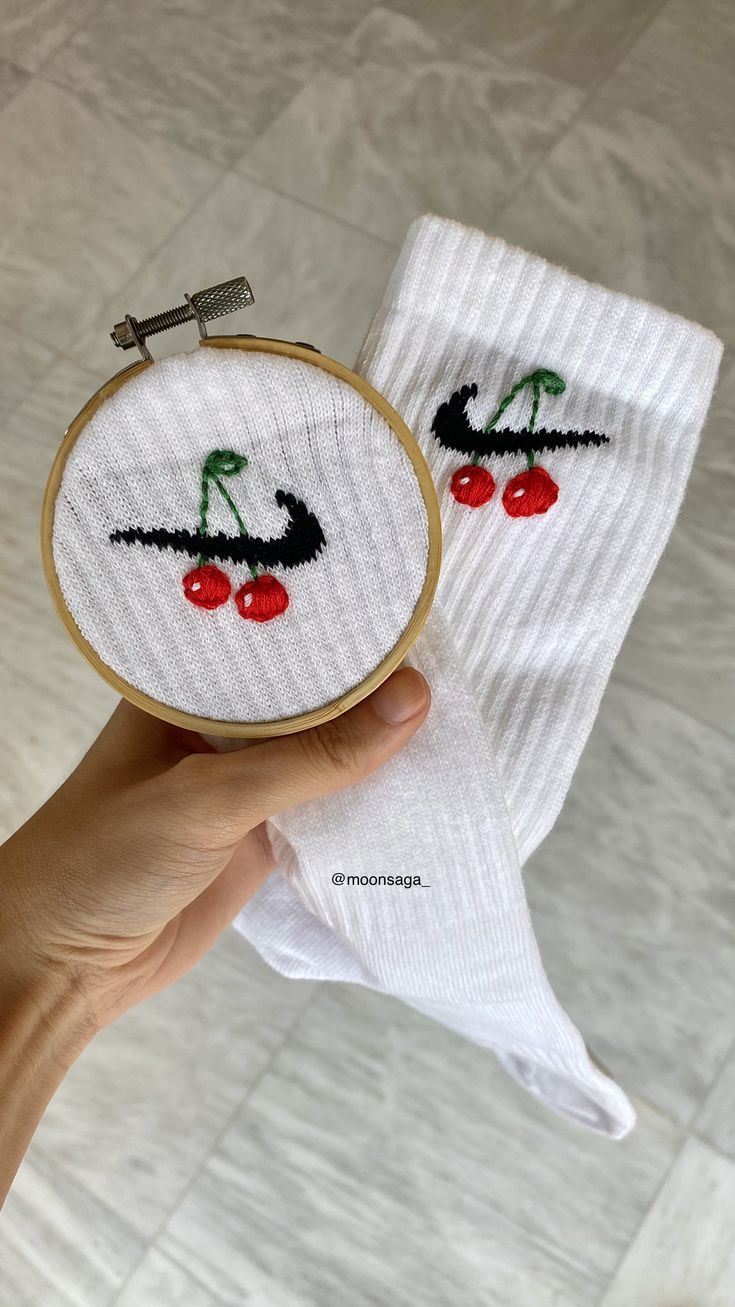 someone is holding up a pair of white socks with cherries on them and one has a needle in it