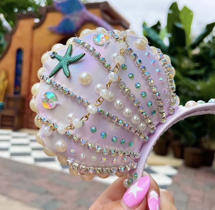 a hand holding a pink seashell with pearls and starfish on it's shell