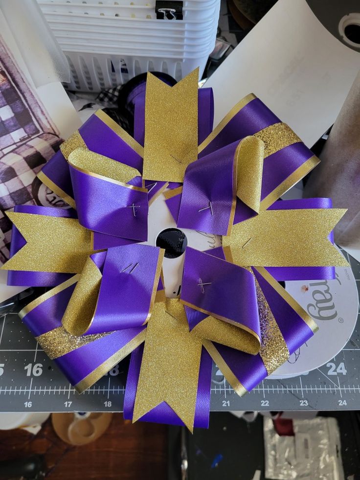 a purple and gold bow sitting on top of a table next to some tape measure