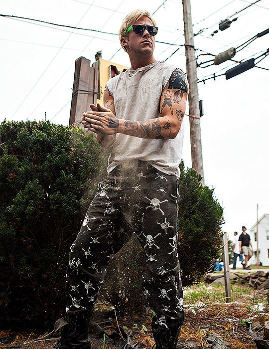 a man with tattoos standing in front of a bush and telephone pole, holding his hands out