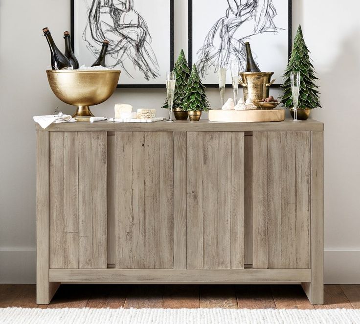 a wooden cabinet with two pictures on the wall behind it and a gold bowl next to it