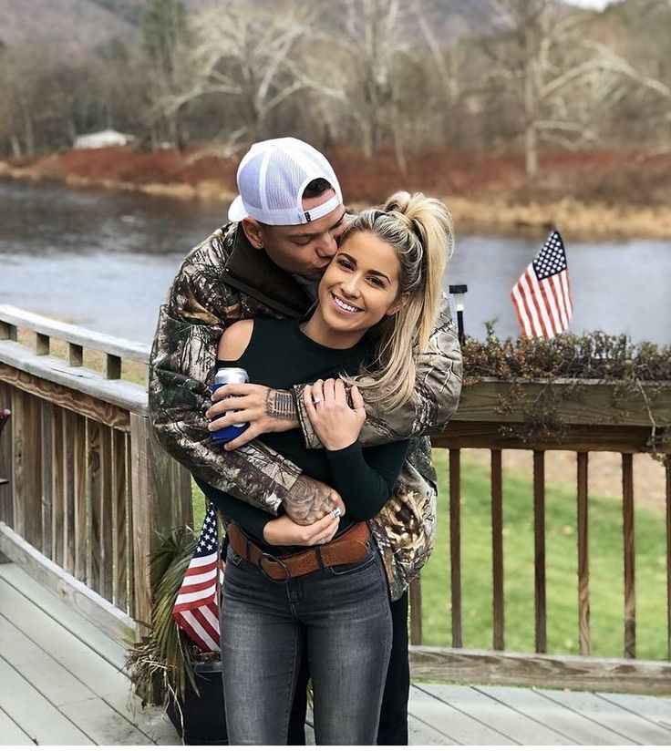 a man and woman hugging each other in front of a lake with an american flag