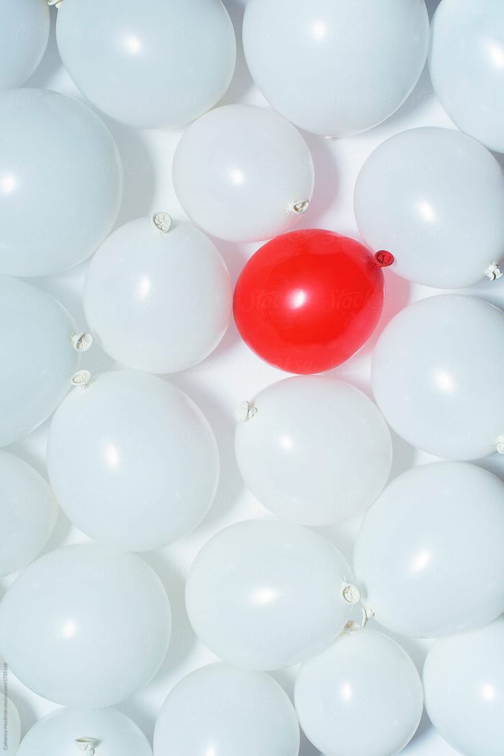 a bunch of white balloons with a red balloon in the middle