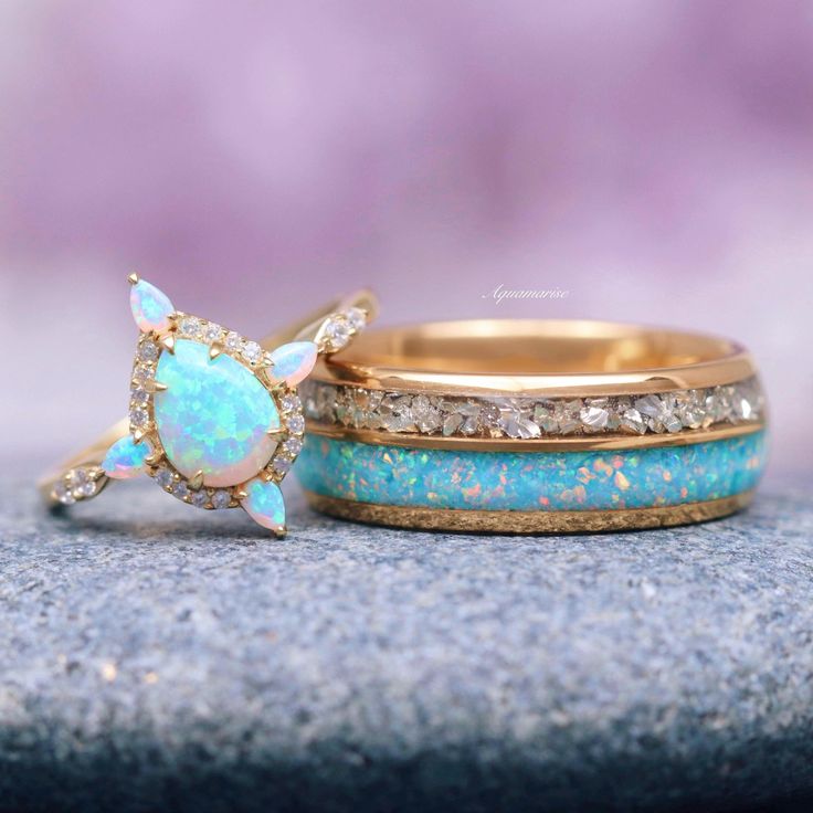 two wedding rings with opal and diamond accents on top of each other, sitting on a rock