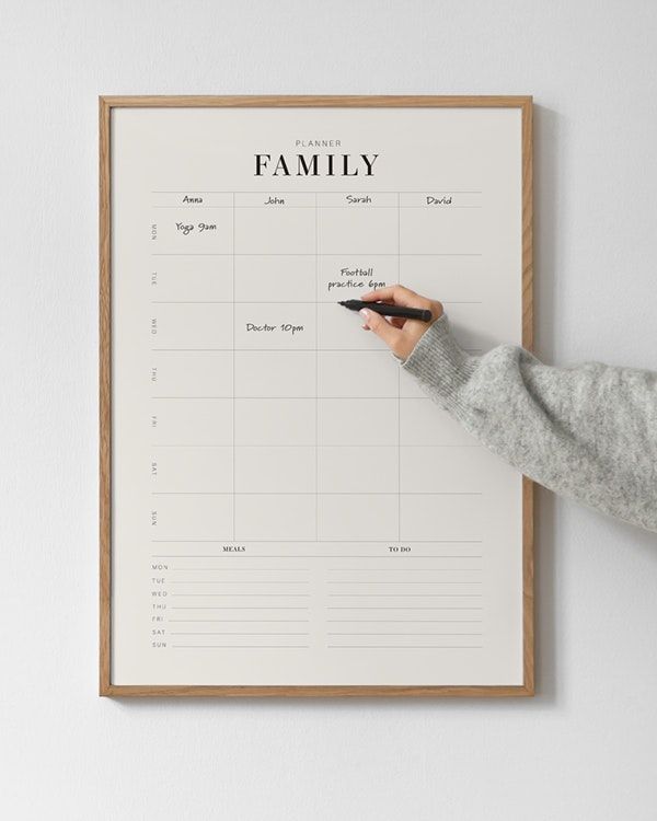 a person writing on a family calendar in front of a white wall with a wooden frame