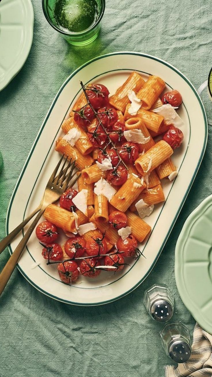 a white plate topped with pasta covered in tomatoes and cheese next to green plates filled with silverware