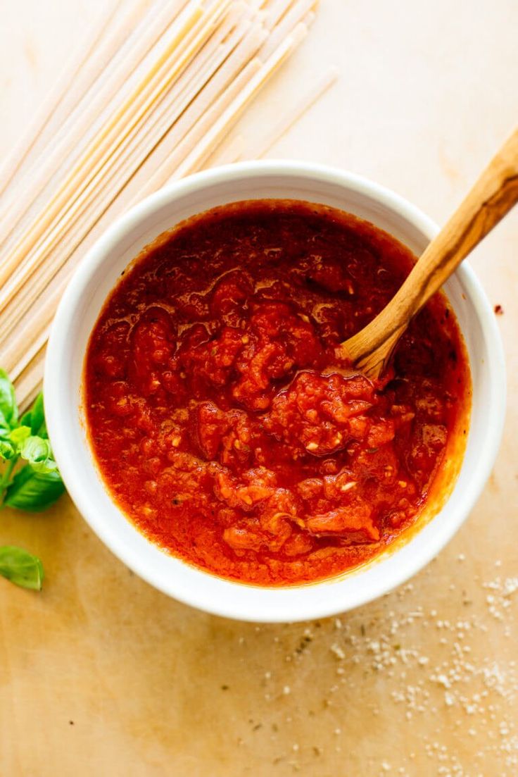 a white bowl filled with tomato sauce next to some chopsticks and parsley