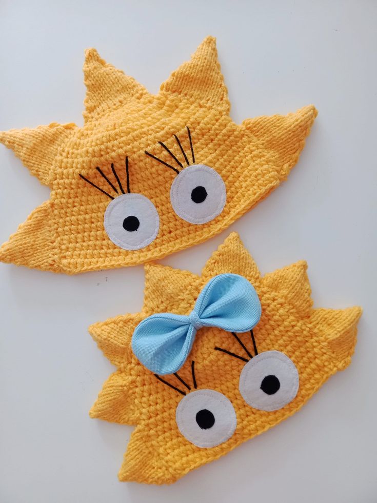 two crocheted hats with eyes and a bow on the top one is made to look like a cat