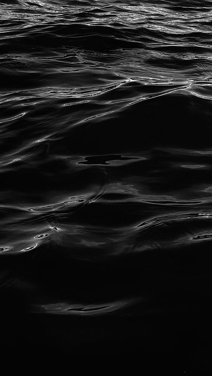 black and white photograph of the ocean water with waves coming in to shore at night