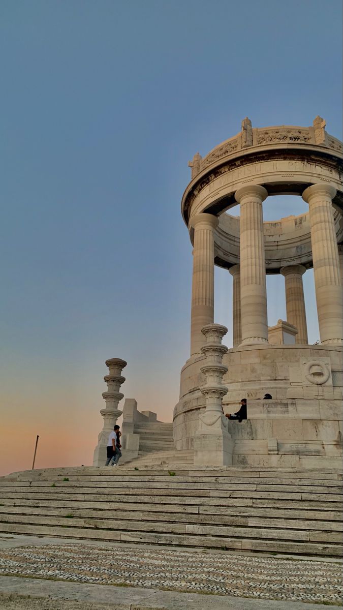 two people are sitting on the steps in front of an old structure with columns and pillars