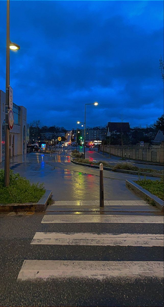 an empty city street at night with rain on the ground and buildings in the background