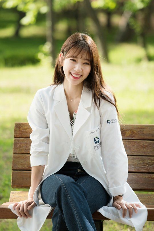 a young woman sitting on top of a wooden bench in a white shirt and jeans