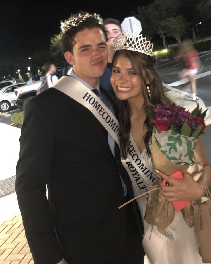 a man standing next to a woman wearing a tiara and holding flowers in her hand