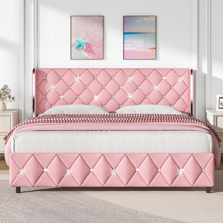 a pink bed in a white room with two pictures on the wall and a rug