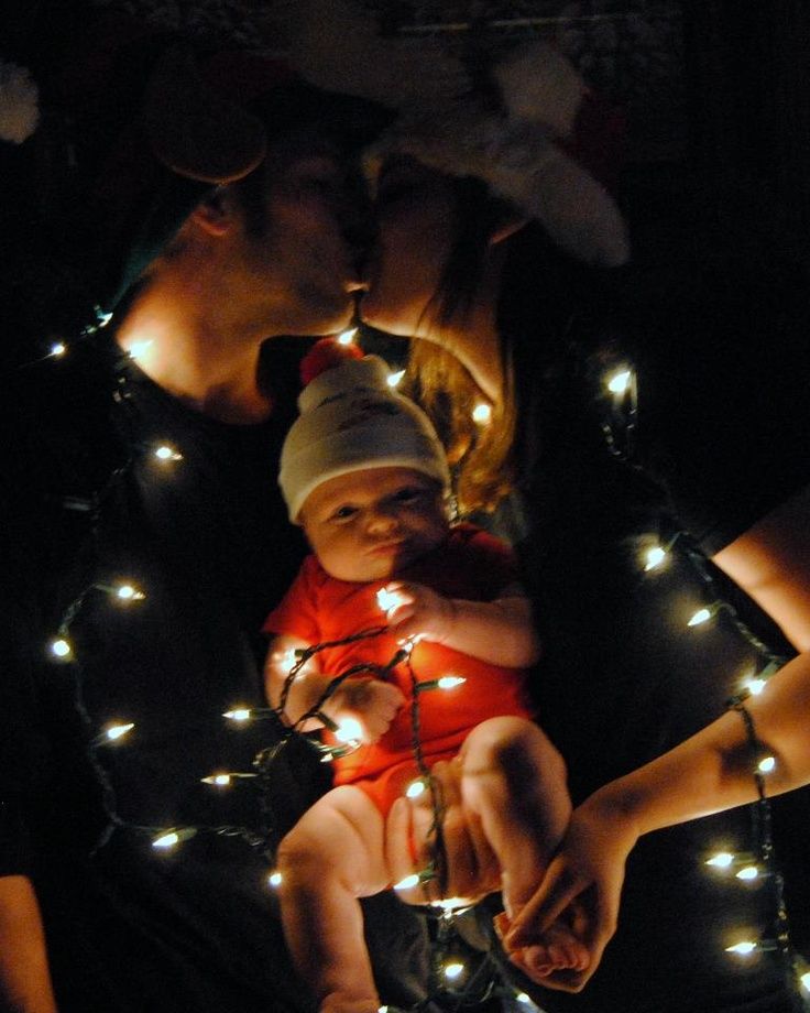 a woman holding a baby in her arms with christmas lights on the ground behind them