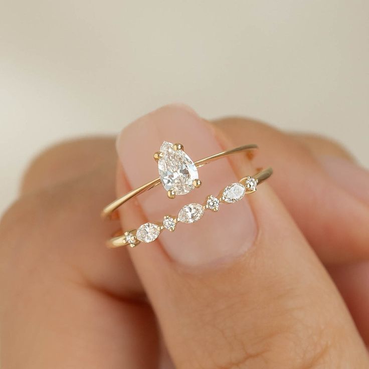 a woman's hand holding a gold ring with two pear shaped diamonds on it