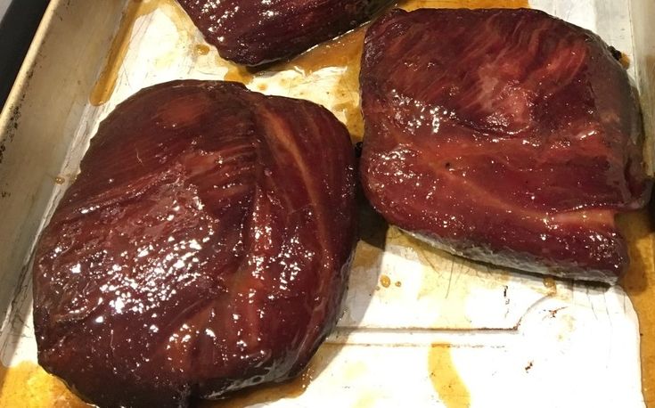 three pieces of raw meat sitting on top of a baking pan covered in brown sauce