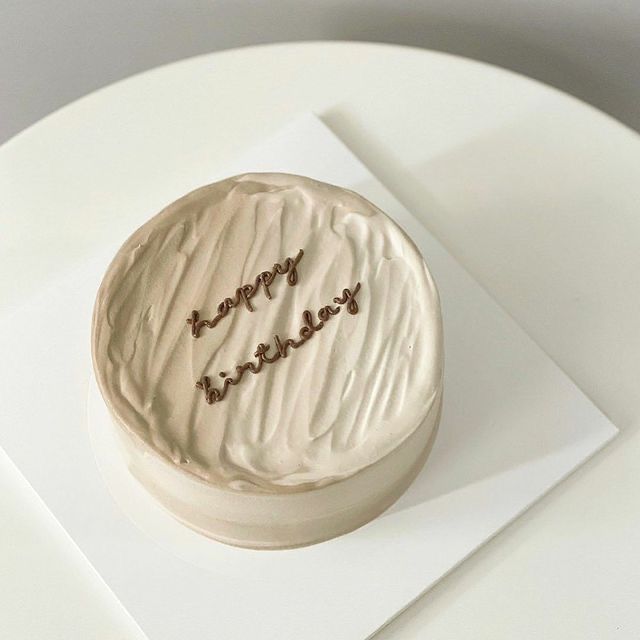 a white cake with writing on it sitting on top of a plate next to a knife and fork