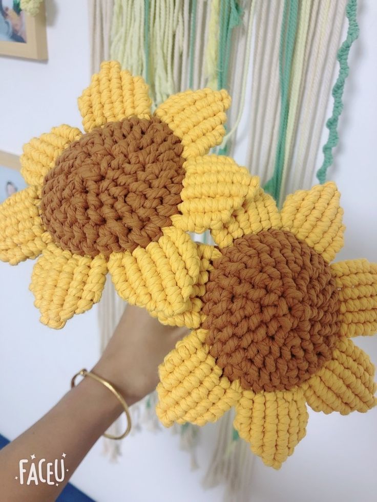 a person holding two knitted sunflowers in front of a wall hanging decoration