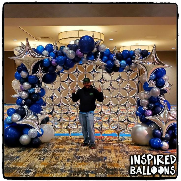 a man standing in front of a balloon arch with blue and silver balloons on it