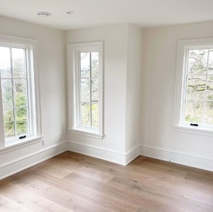 an empty room with three windows and hard wood flooring