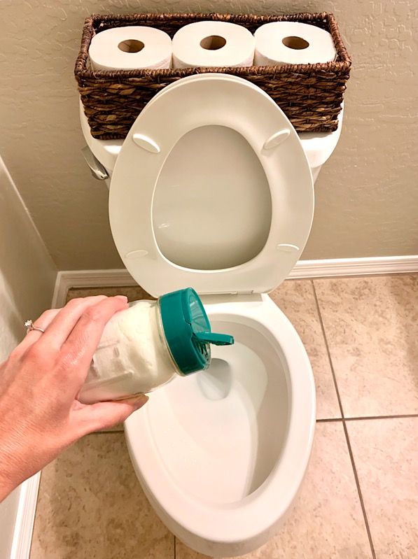 a person is cleaning the toilet with a spray bottle and two rolls of toilet paper