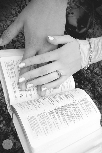 two hands on top of an open book with the pages folded down and their fingers touching each other