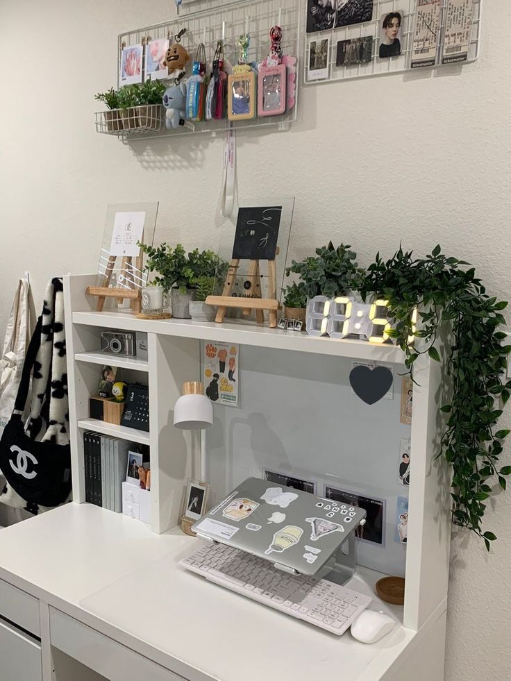 a white desk topped with a laptop computer next to a shelf filled with books and plants