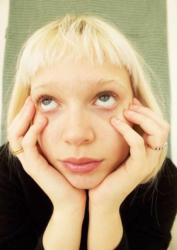 a woman with blonde hair and blue eyes holding her hands to her face while looking at the camera