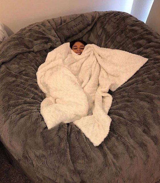 a person wrapped in a blanket on top of a bean bag chair that's been turned into a bed