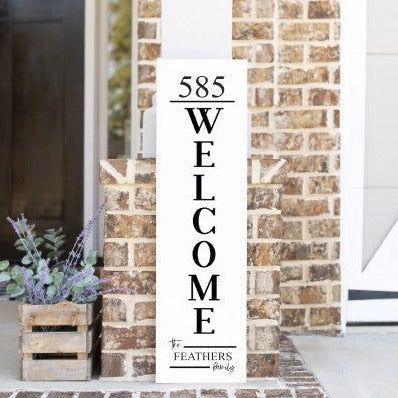 a welcome sign sitting in front of a brick building next to a potted plant