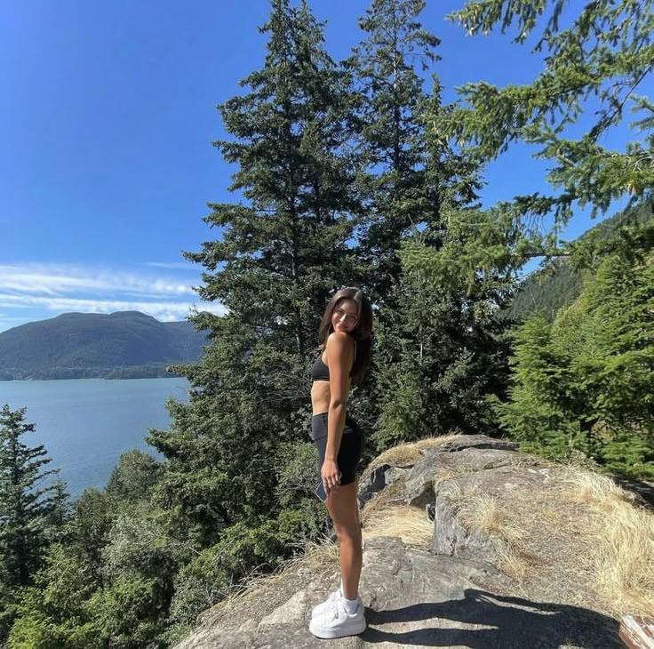 a woman standing on top of a rock next to trees and the ocean in the background