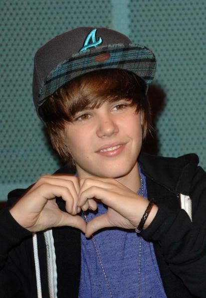 a young man making a heart shape with his hands while wearing a hat and jacket