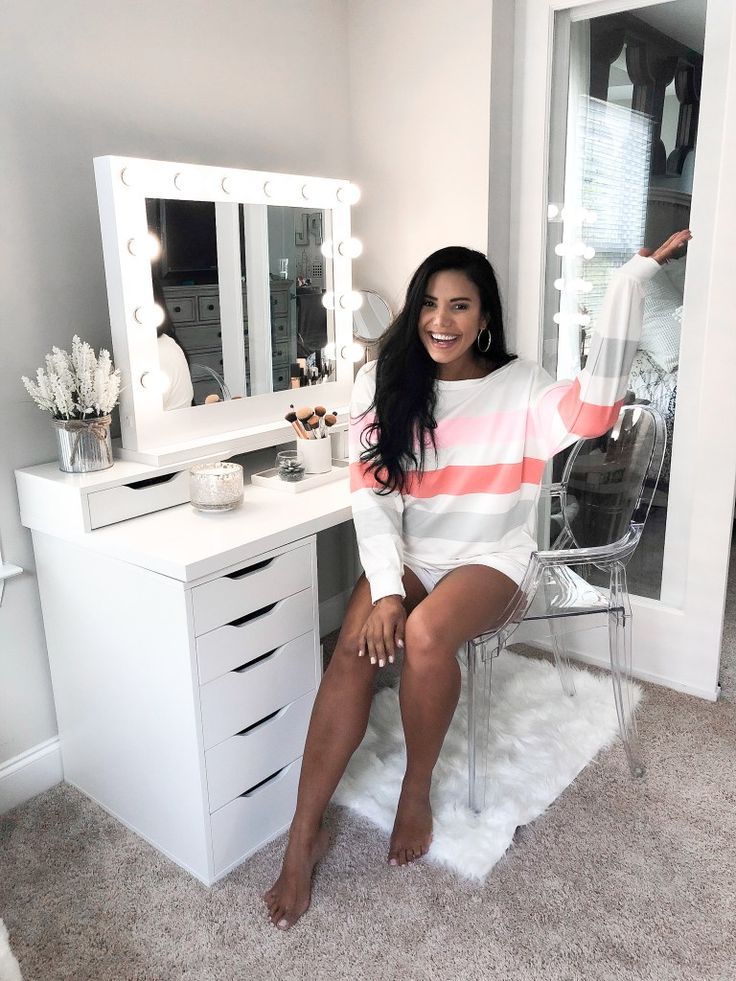 a woman sitting on a chair in front of a dressing table with a mirror and lights