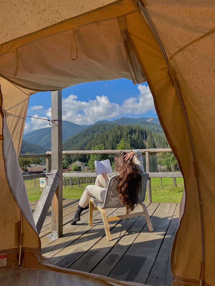 a woman sitting in a chair on top of a wooden deck next to a tent