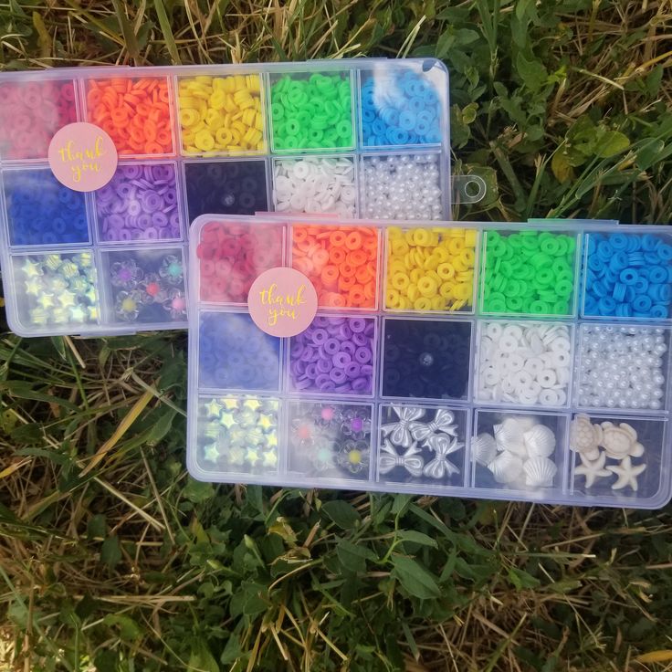 two plastic trays filled with different colored beads on top of green grass next to each other