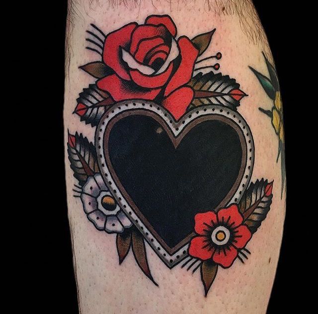 a black heart with red roses and leaves on the side of a man's leg