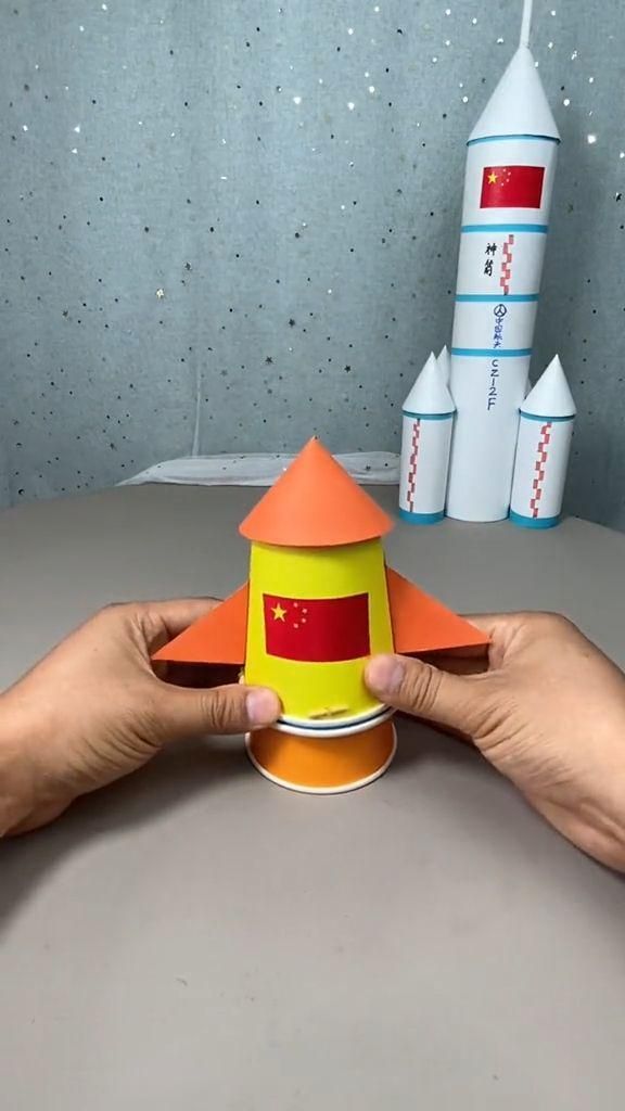 two hands holding a paper model of a rocket ship and another hand reaching for it