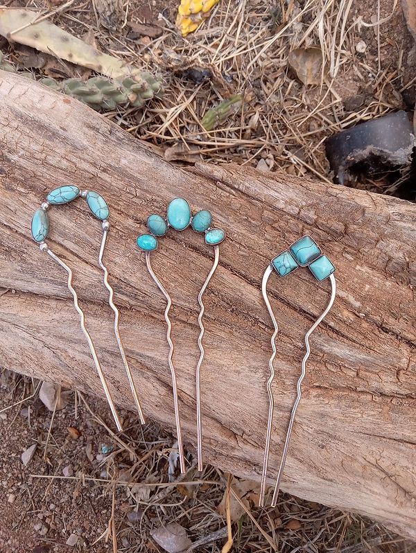 four hair pins with turquoise stones on them sitting on a piece of wood in the woods