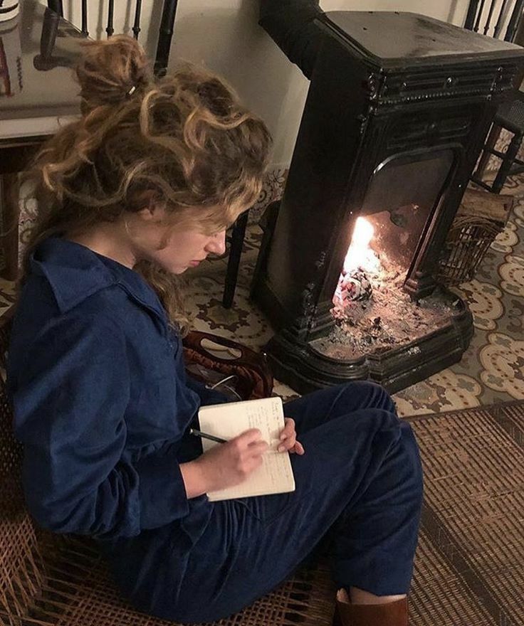 a woman sitting on the floor in front of a fire place reading a notepad