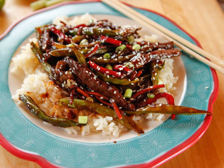 a blue and red plate topped with rice covered in stir fried vegetables next to chopsticks