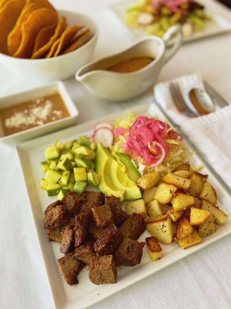 a white plate topped with meat and veggies next to bowls of dipping sauce