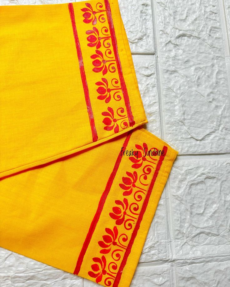 two pieces of yellow cloth with red and gold designs on the edges, sitting against a white brick wall