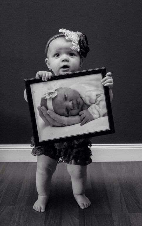 a black and white photo of a baby holding up a framed photograph with her hands