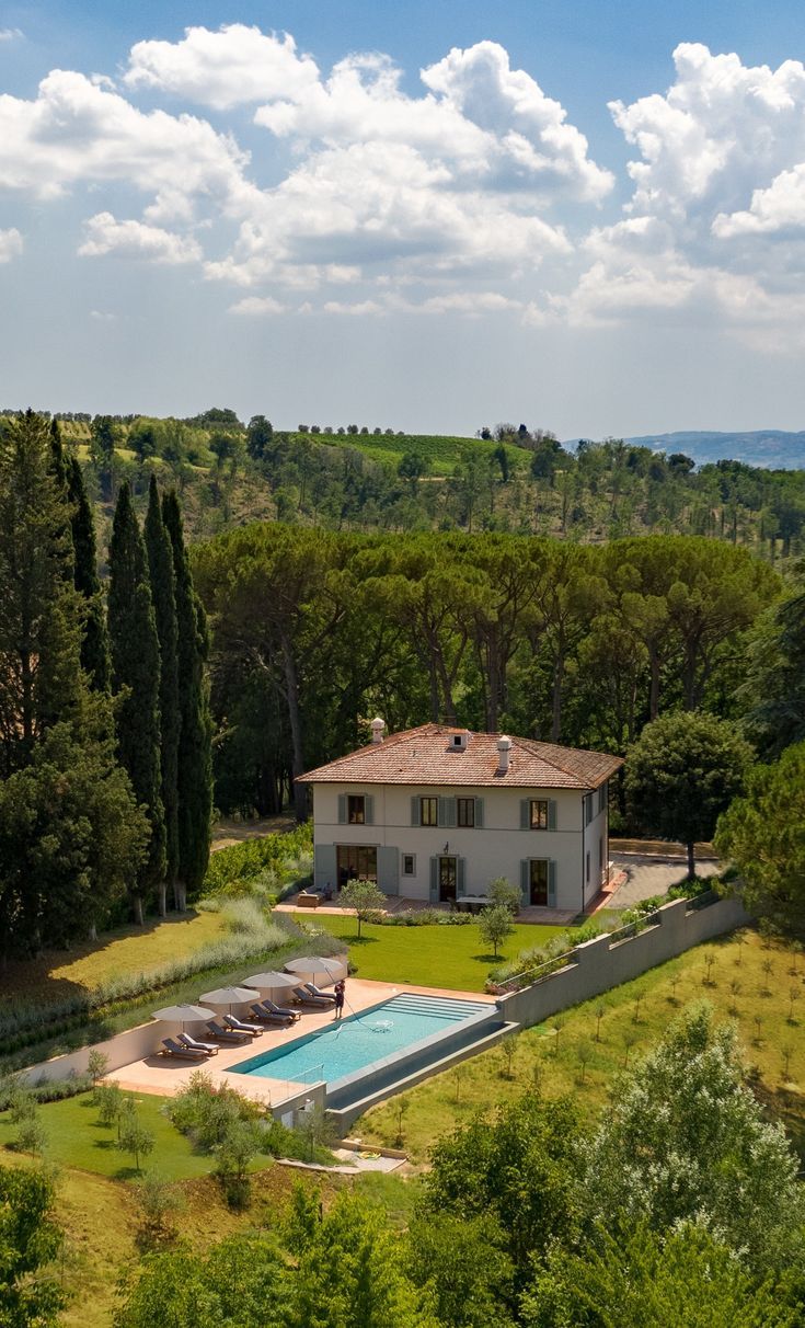 an aerial view of a house with a pool in the foreground and trees surrounding it