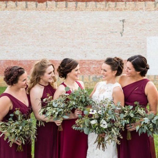 a group of women standing next to each other in front of a brick wall holding bouquets