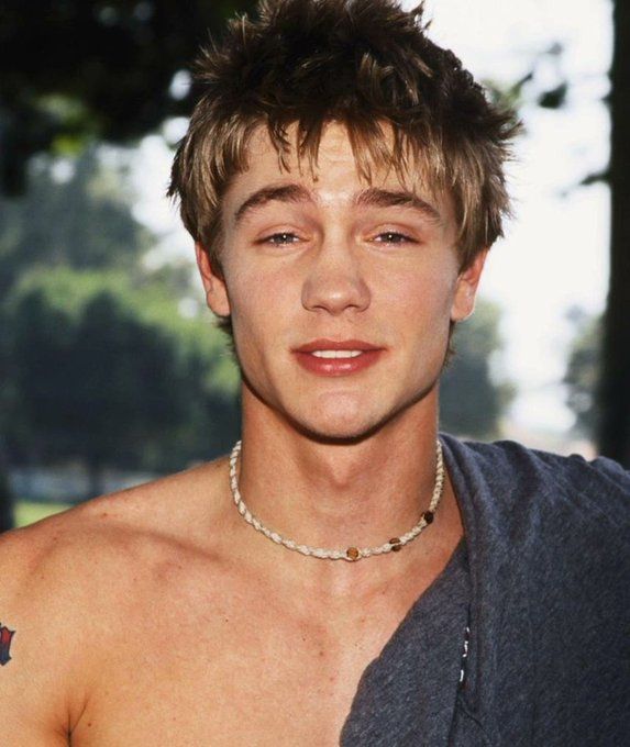 a shirtless young man wearing a chain around his neck is looking at the camera