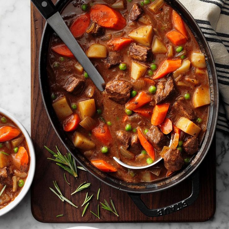 a pot filled with stew and carrots on top of a wooden cutting board next to a white plate