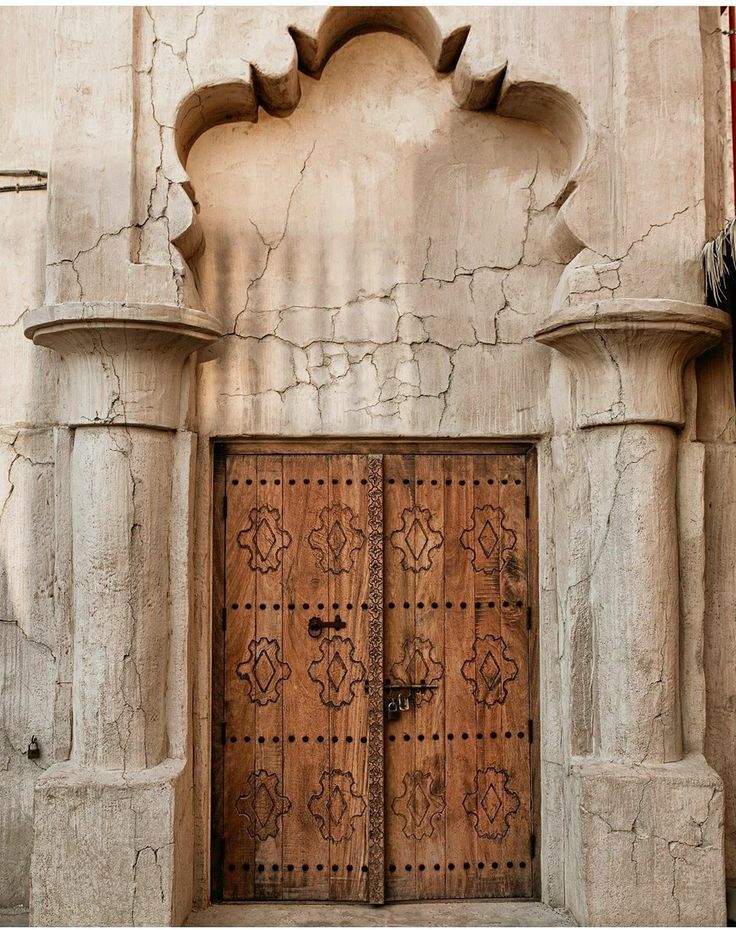 two wooden doors in an old building with stone pillars and carvings on the outside wall